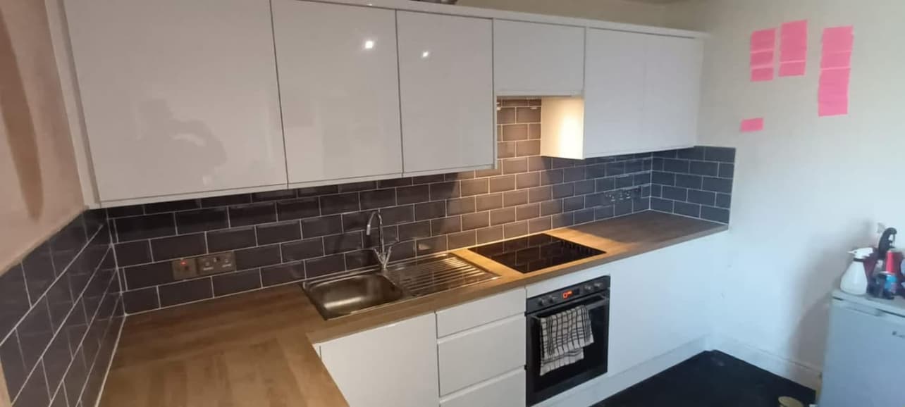 After — finished kitchen with gloss units, dark metro tiles and timber worktops